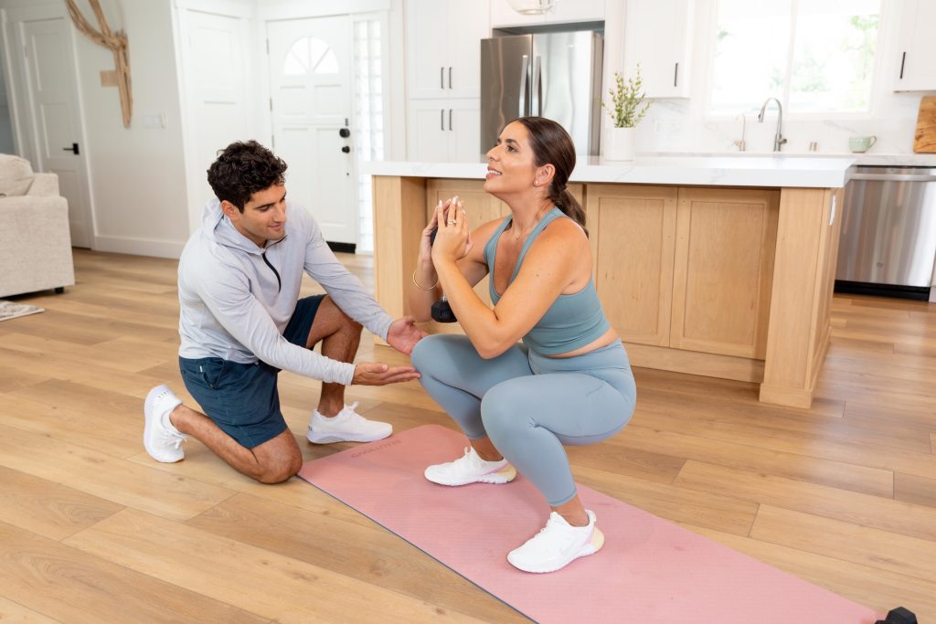 Tallene doing a squat exercise on her yoga mat and Sirak pointing to her knee to show proper form