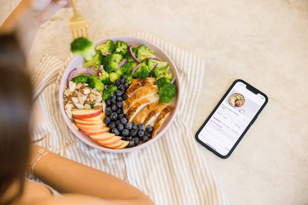 bowl of grilled chicken, blueberries, broccoli, and sliced almonds next to a phone showing the recipe