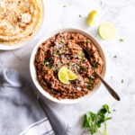 A bowl of refried beans topped with minced garlic, cilantro, and lime wedges.